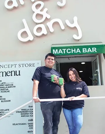Andrea y Daniel, Andy y Dany, sonriendo con dos matchas frente a la ventanita MATCHA BAR