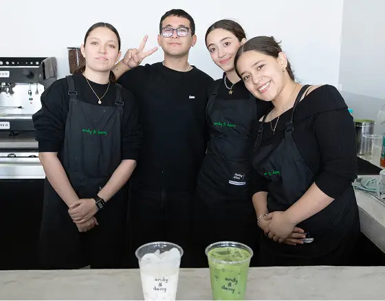 Cuatro integrantes del equipo de andy & dany con sus mandiles, sonriendo detrás de la barra junto a dos bebidas